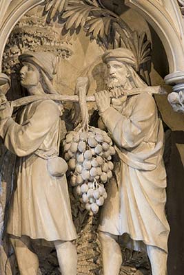 Stone carving of two figures carrying a large cluster of grapes.